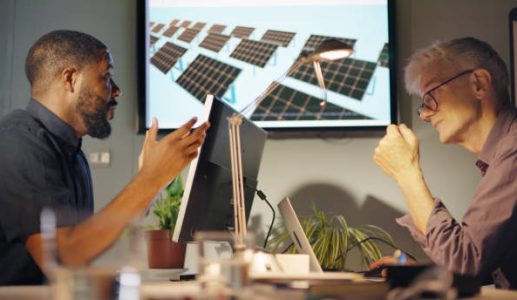 Stock image of two men, one black and the other white & mature meeting to discuss solar pale installation design… this is shown on a screen in the office.
